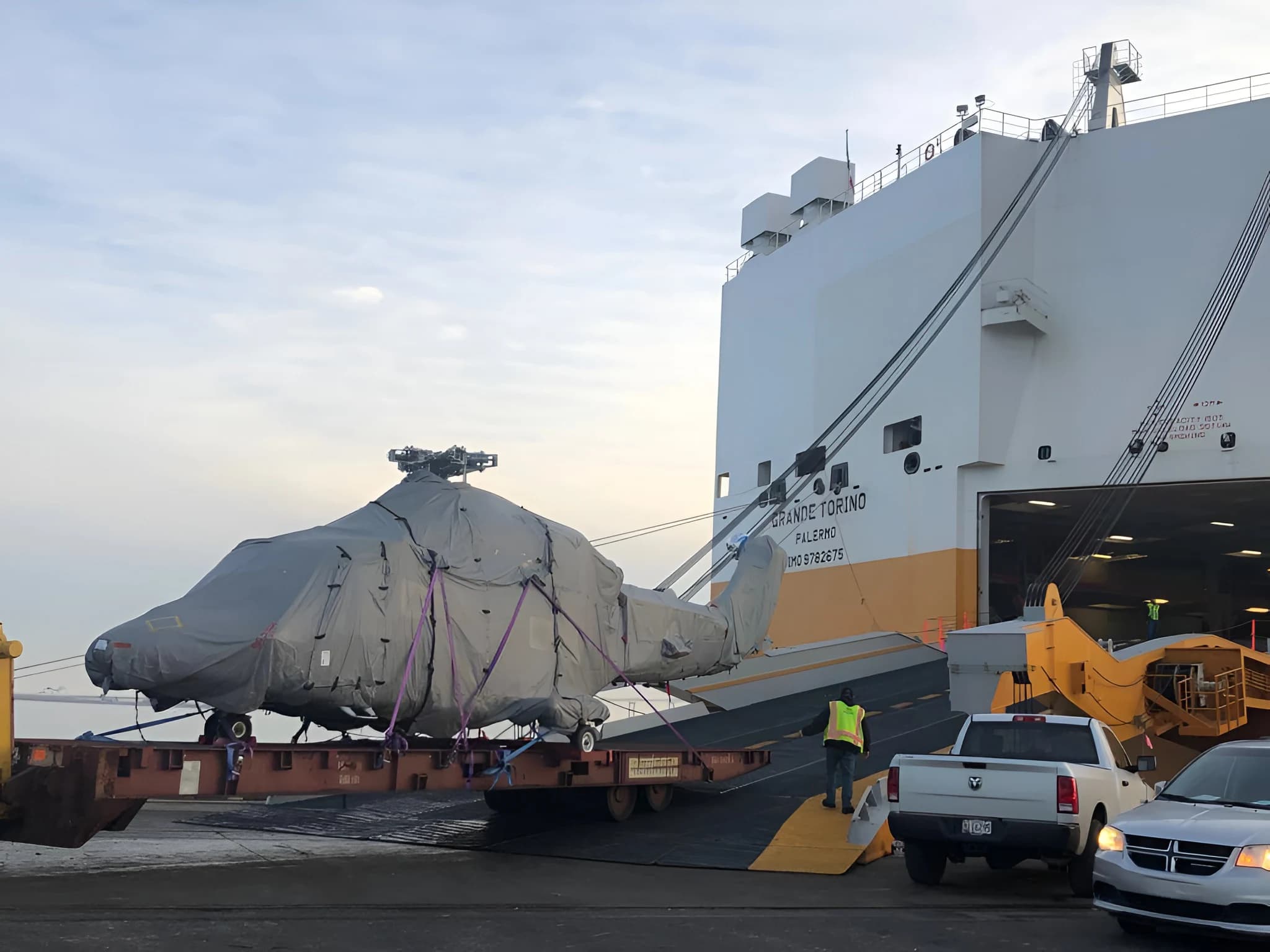 Wrapped helicopter being lifted by ship-side crane